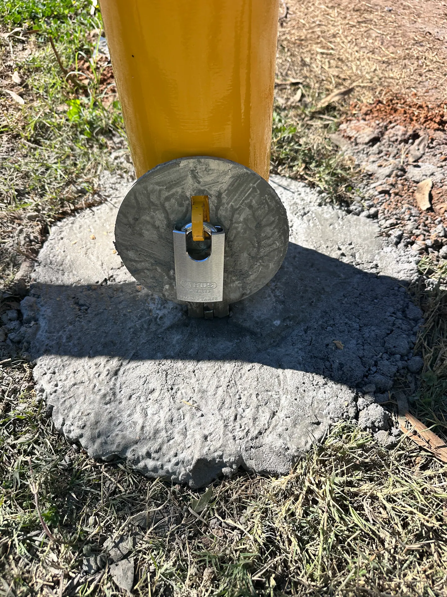 A secured yellow access bollard installed in a concrete footing