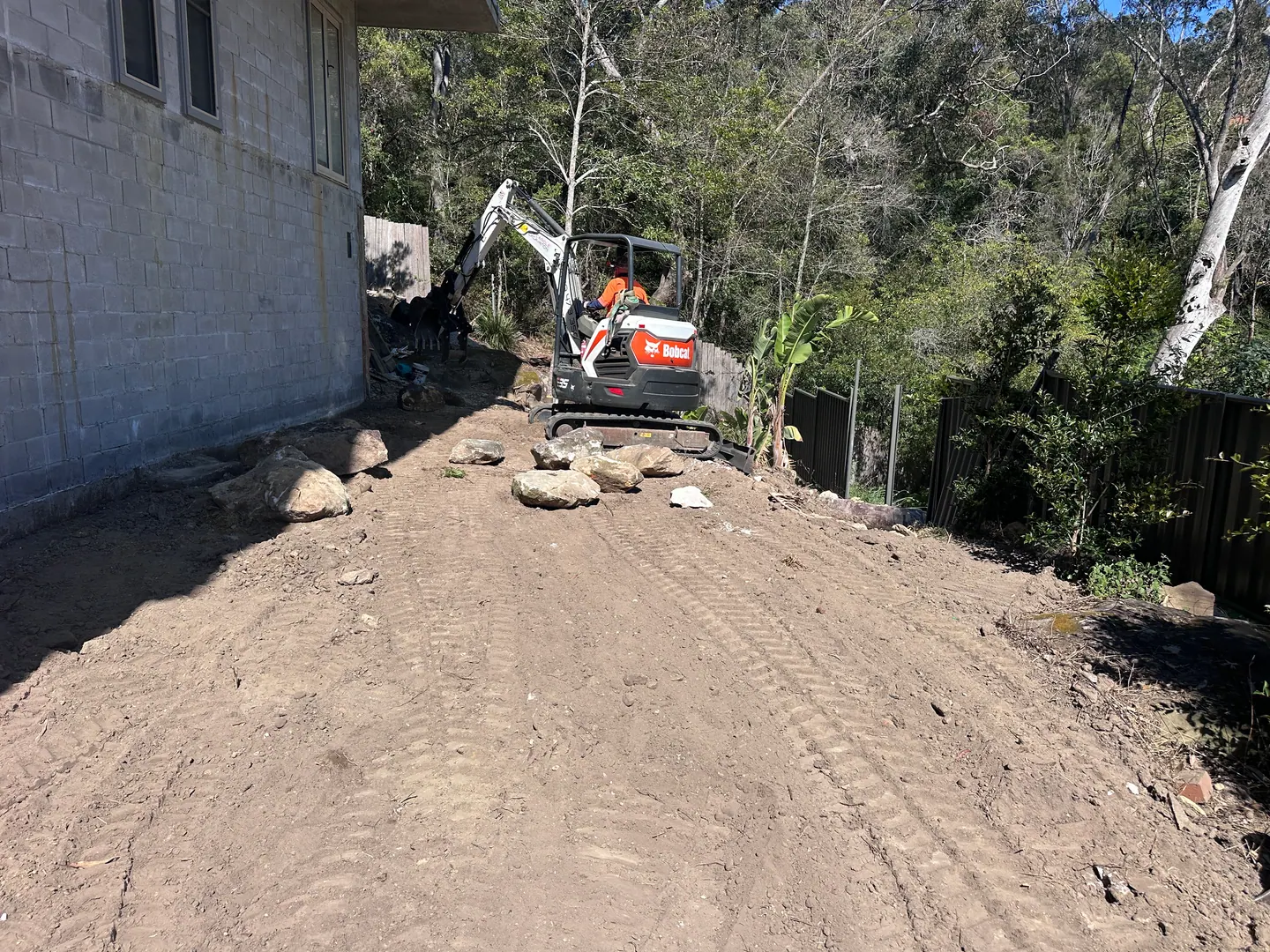 Ground preparation beside a residential building with an excavator on site
